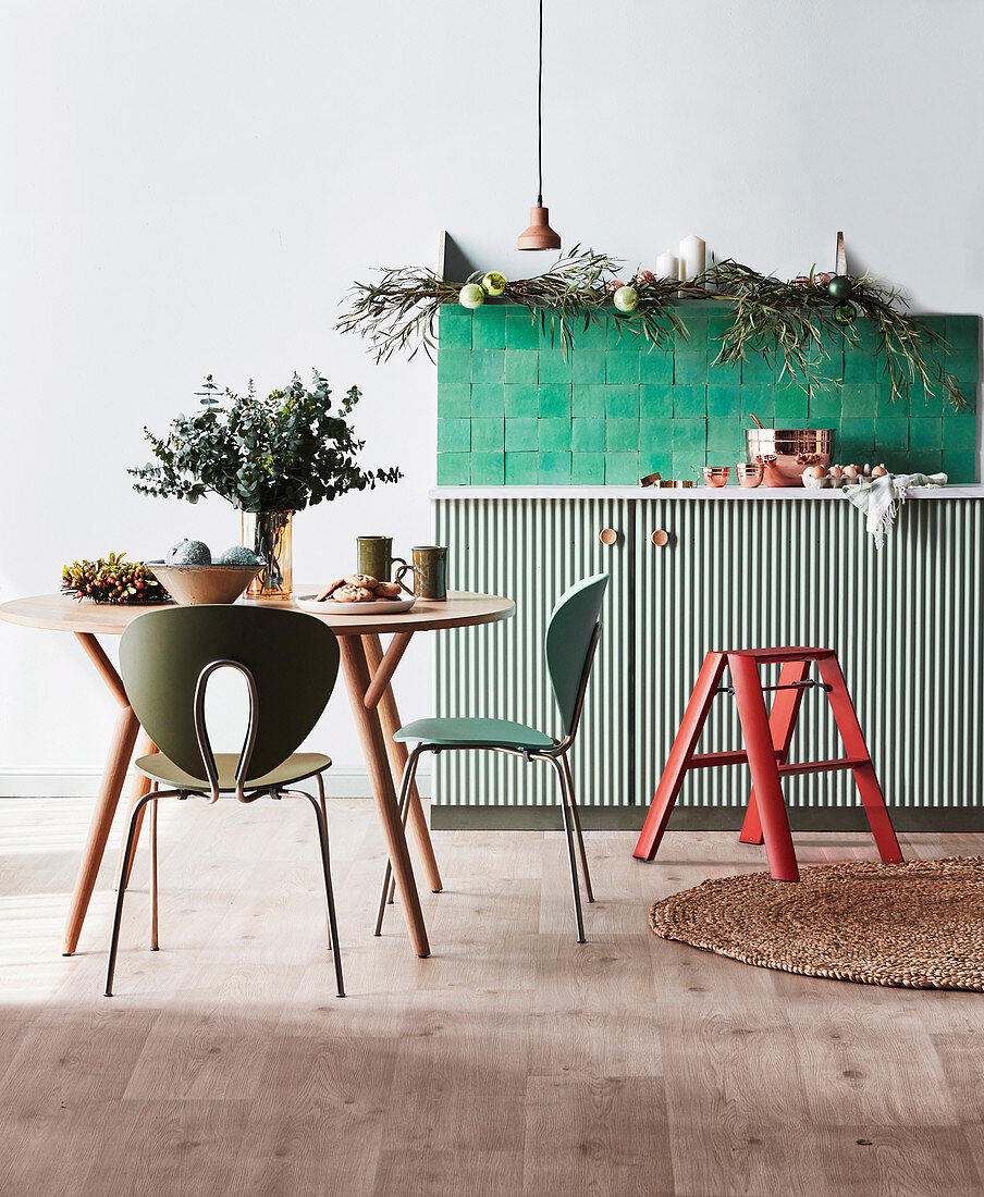 Runder Tisch mit Stühlen und grüne Fliesen über Unterschrank in weihnachtlich dekorierter Küche