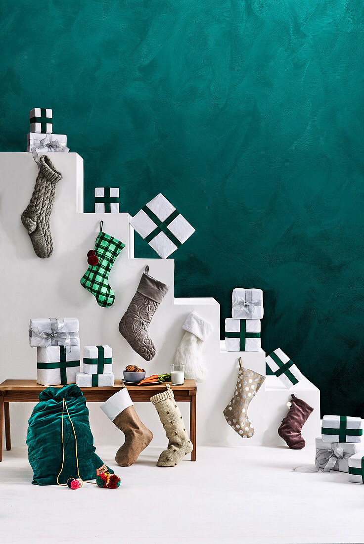 Weiße Treppe mit Weihnachtsgeschenken und Nikolausstrümpfen dekoriert vor grüner Wand
