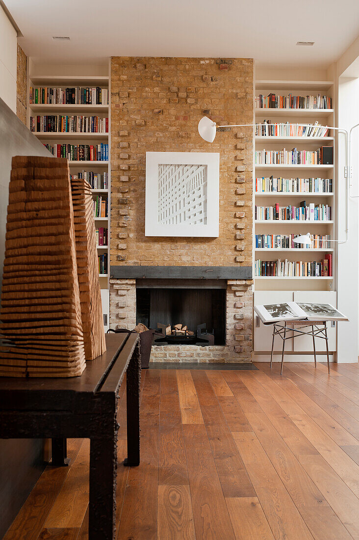 Two wooden sculptures on table and open fireplace flanked by fitted bookcases