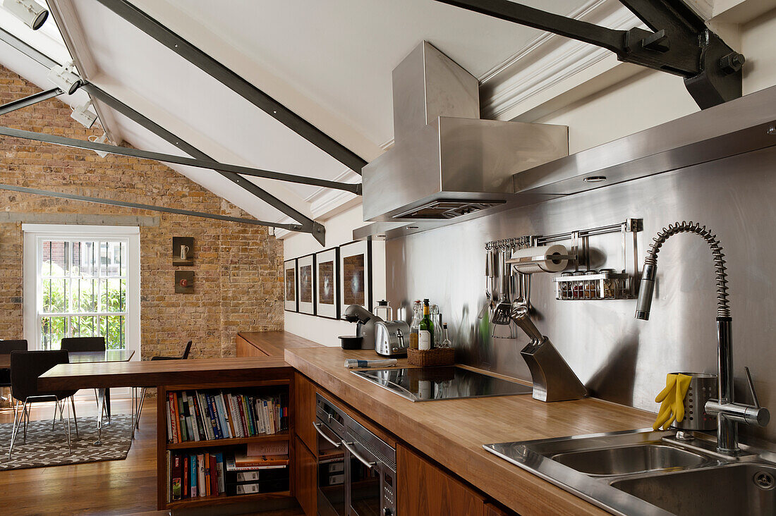 Open-plan kitchen below open roof structure with cross-members and brick wall