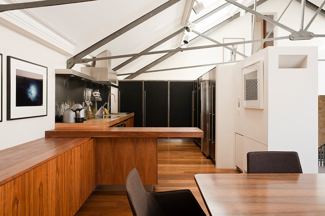 Wooden cupboards in open-plan kitchen of renovated loft apartment with sloping ceiling and cross-members