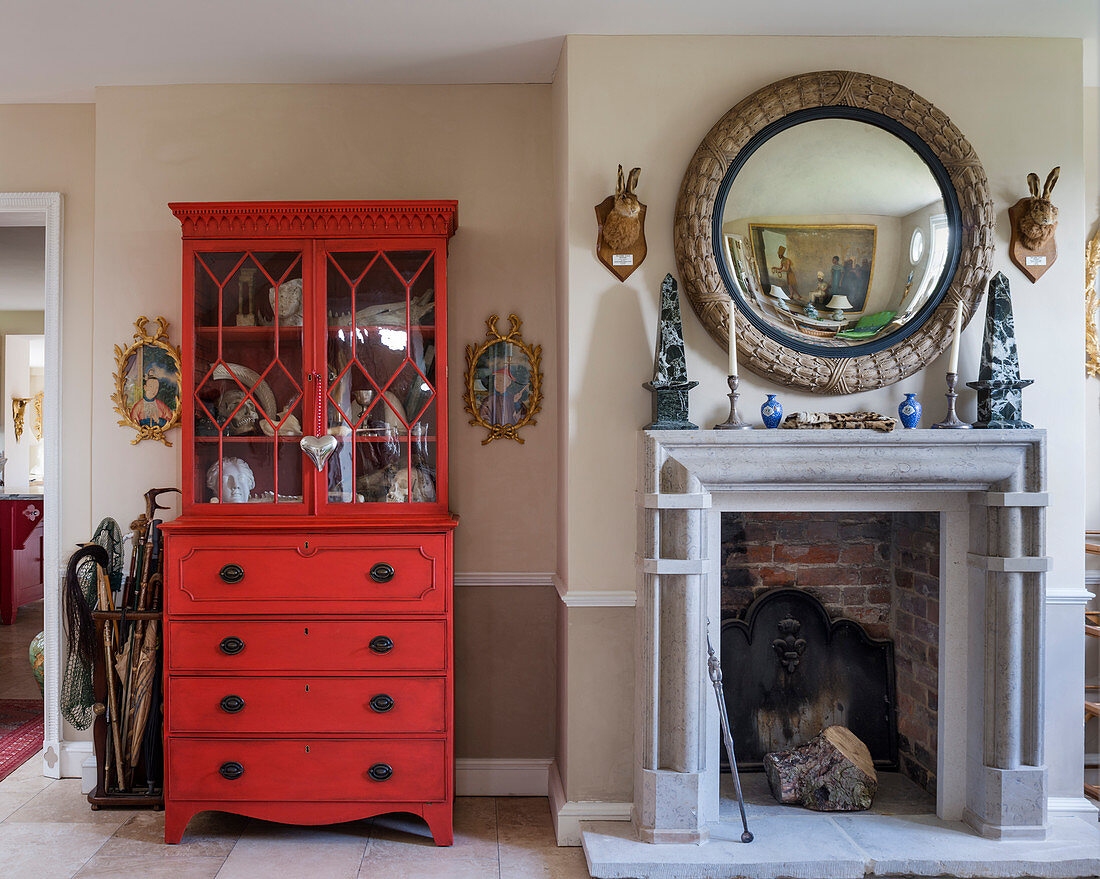Red-painted mahogany dresser next to round mirror above fireplace