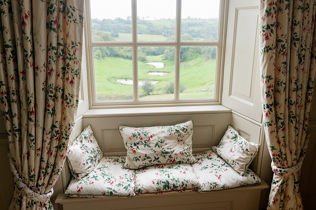Sitzbank in Fensternische mit geblümten Kissen und Vorhängen