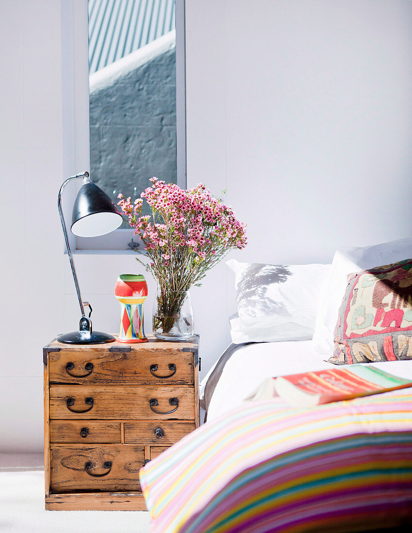 Antique, Asian chest of drawers as a bedside table next to a double bed in a bright bedroom