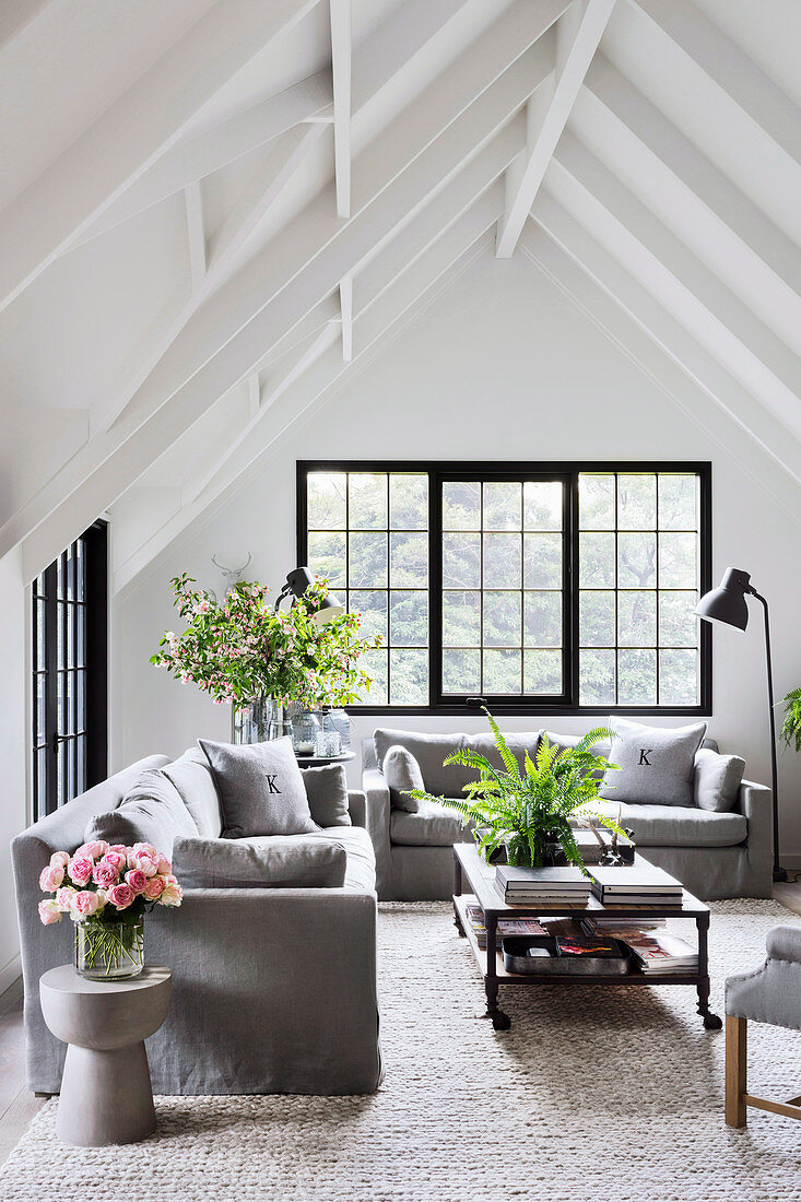 Heller Wohnraum unter weißem Giebeldach mit grauen Sofas und schwarzen Sprossenfenstern