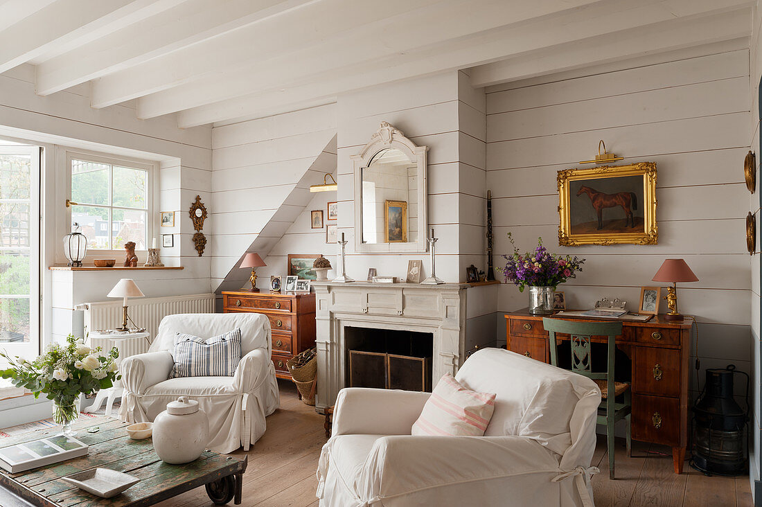 Weiße Hussensessel und Couchtisch auf Rädern vor Kamin im Wohnzimmer mit weiß gestrichenen Holzwänden