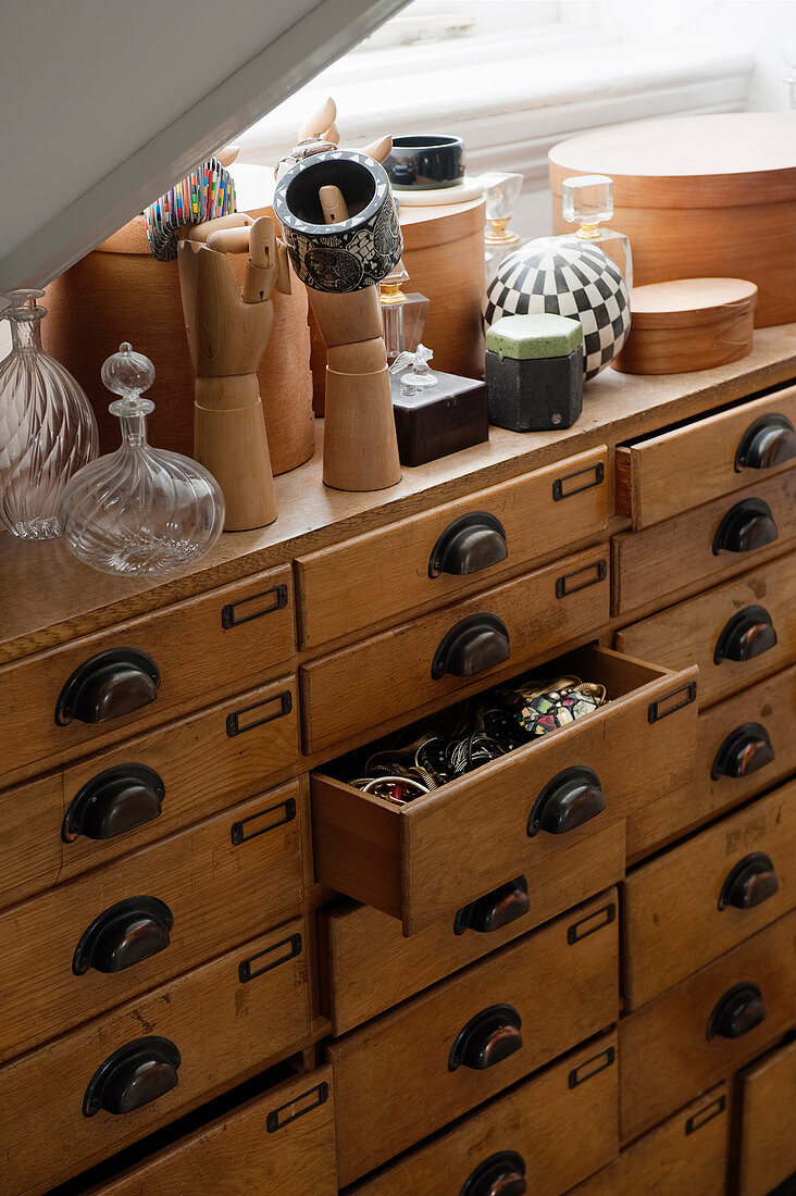 Boxes, bottles and mannequin hands on top of antique haberdasher's chest of drawers