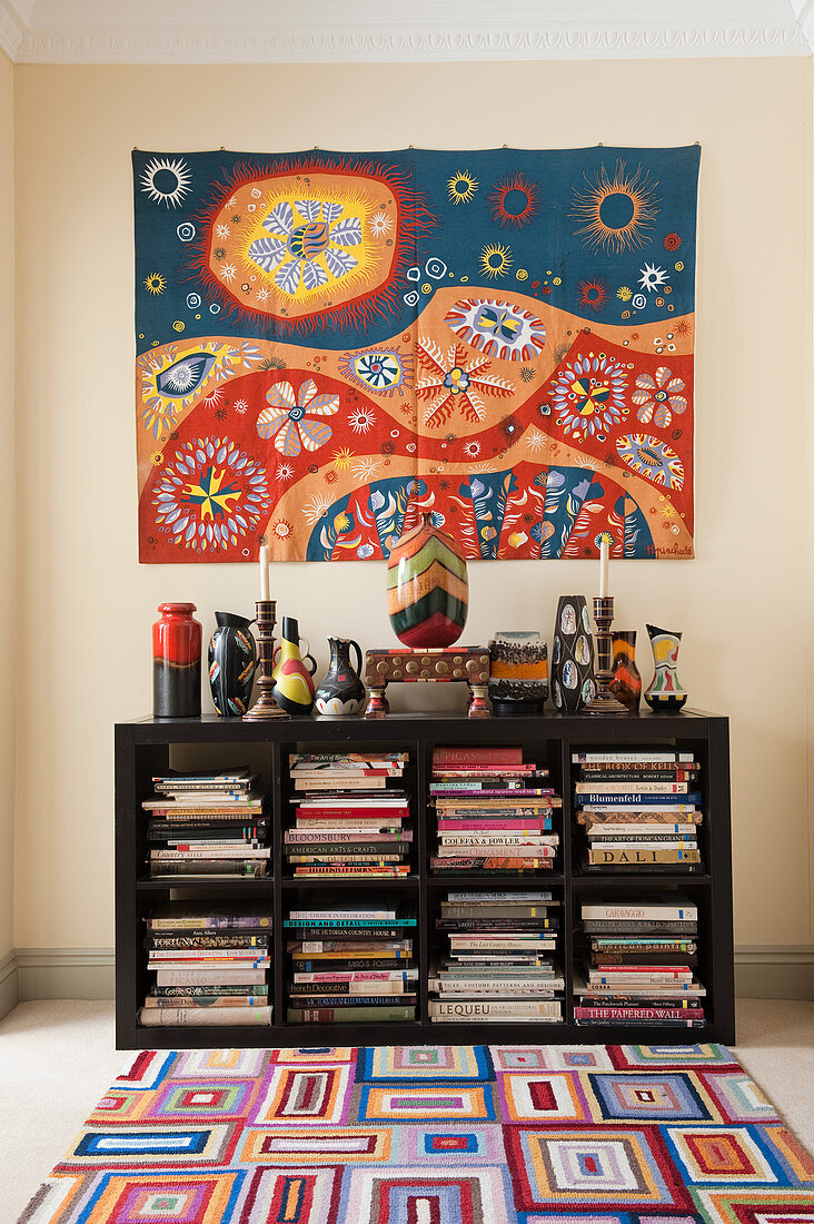 Mexican wall-hanging above collection of artistic vases on bookcase