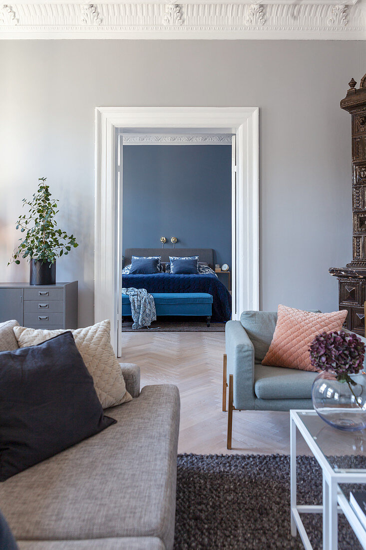 View through double doors into bedroom with grey-blue walls, bed and bedroom bench