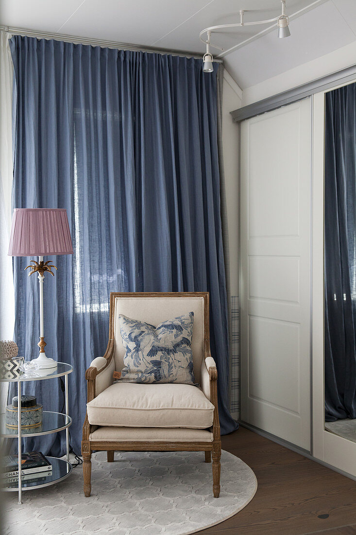Klassischer Polsterstuhl vor blauem Vorhang im Schlafzimmer