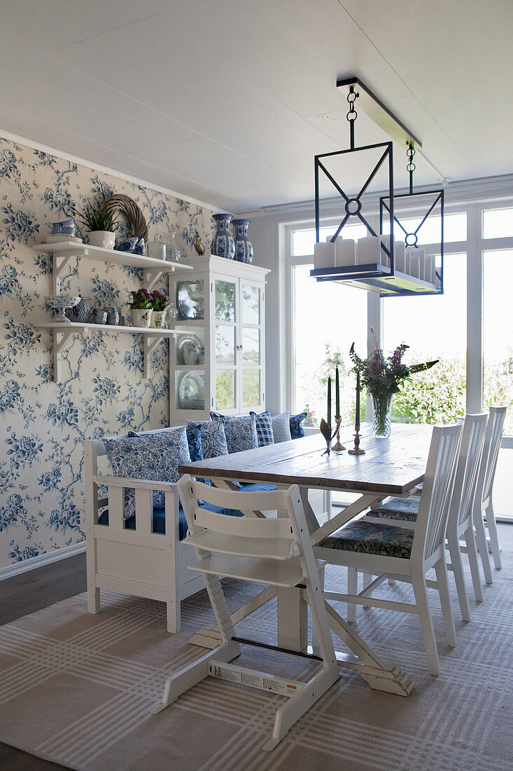 High chair at table in open-plan dining room with floral wallpaper