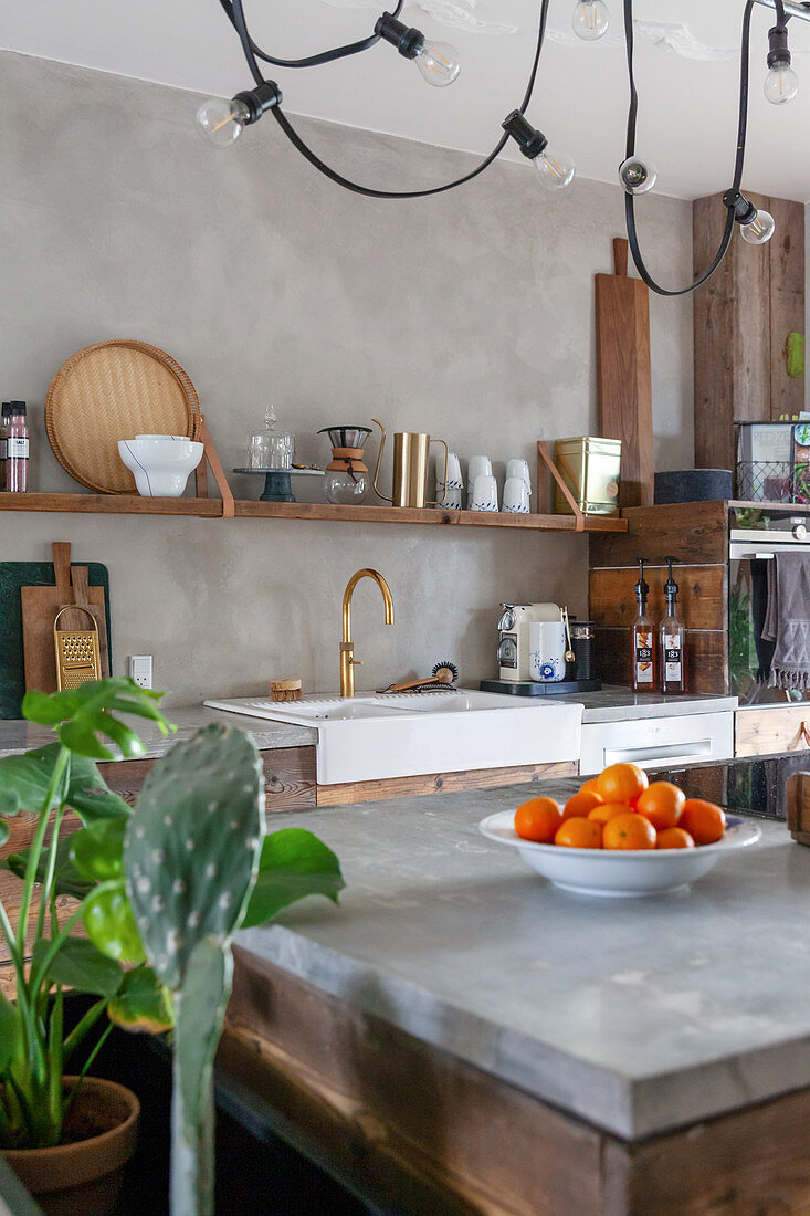 Blick über Kücheninsel mit Betonplatte auf Spülbecken und Regal