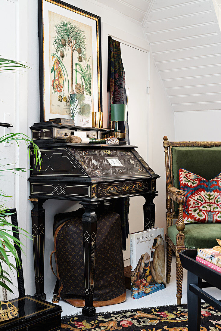 Black, antique bureau with inlay work next to green velvet armchair