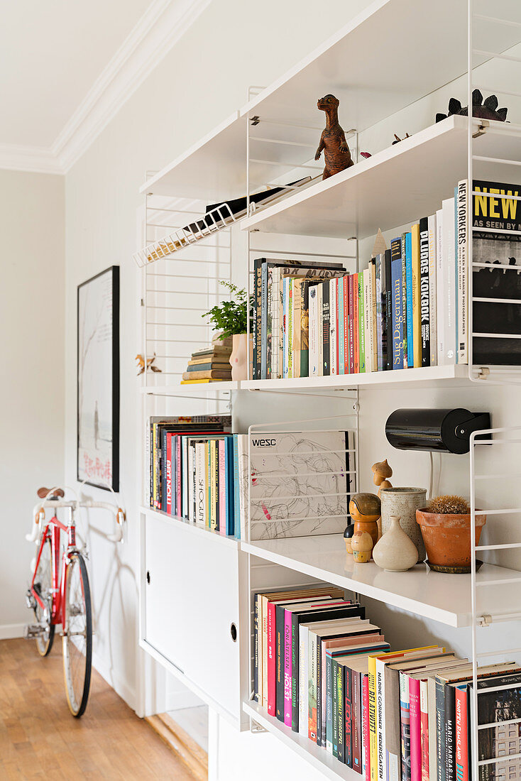 Weiße Regale mit Büchern und Dekoobjekten und Fahrrad im Wohnzimmer
