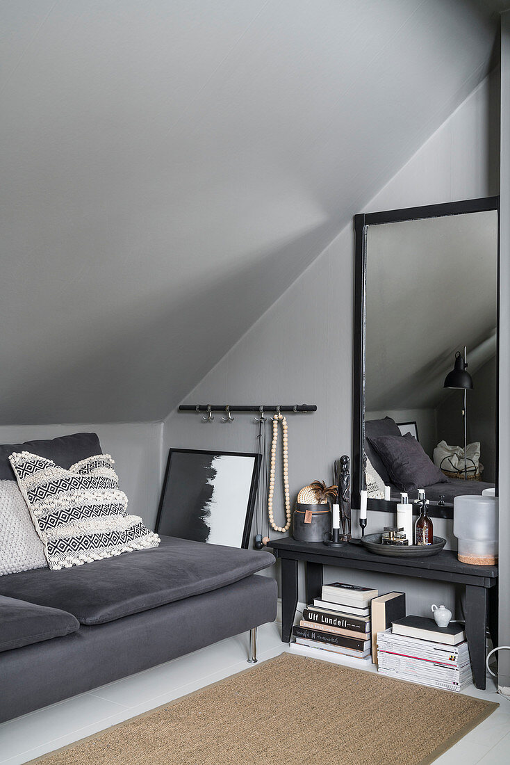 Sofa, side table and mirror on wall under grey, sloping ceiling