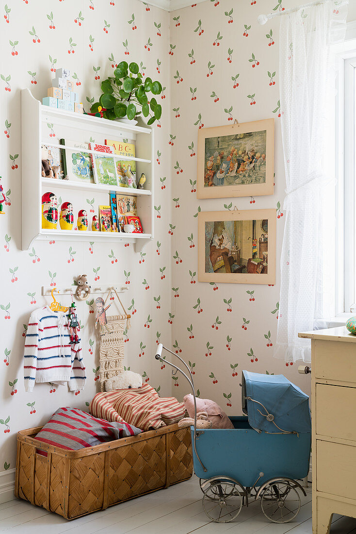Old dolls' pram in child's bedroom with cherry-patterned wallpaper