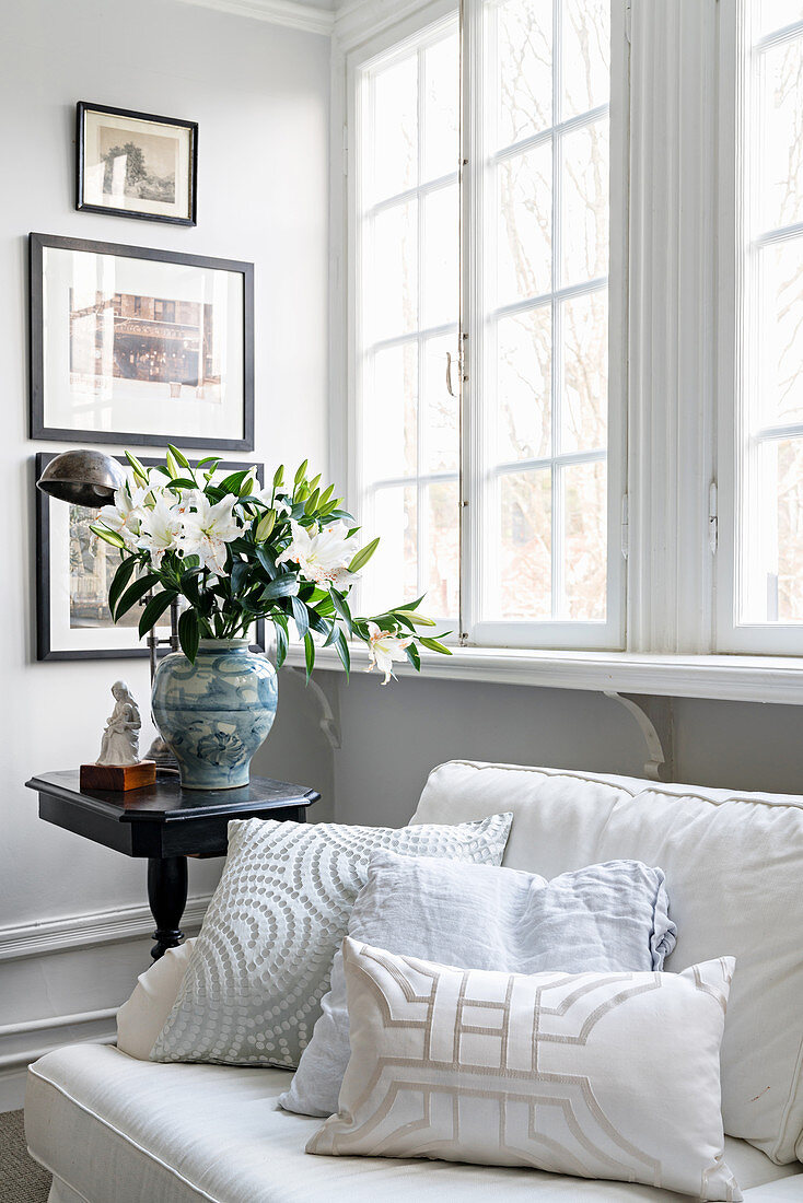 Scatter cushions on sofa and vase of lilies on side table next to lattice window