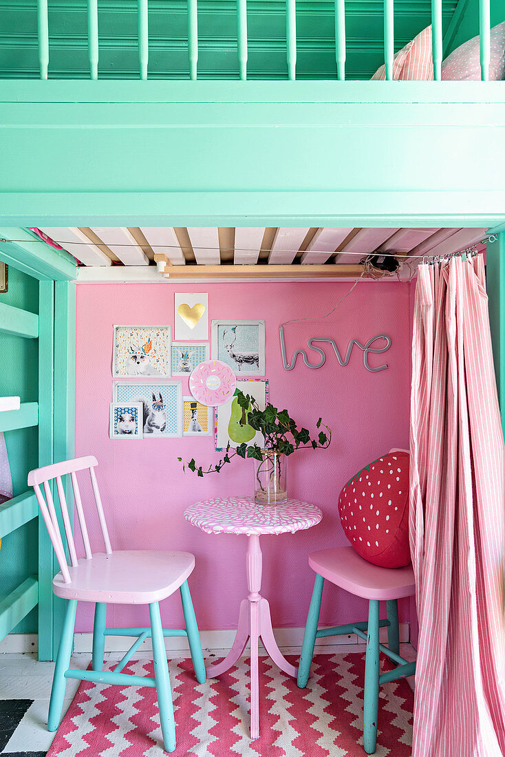 Zwei Stühle und Tisch vor pinkfarbener Wand, darüber Hochbett im Spielhaus