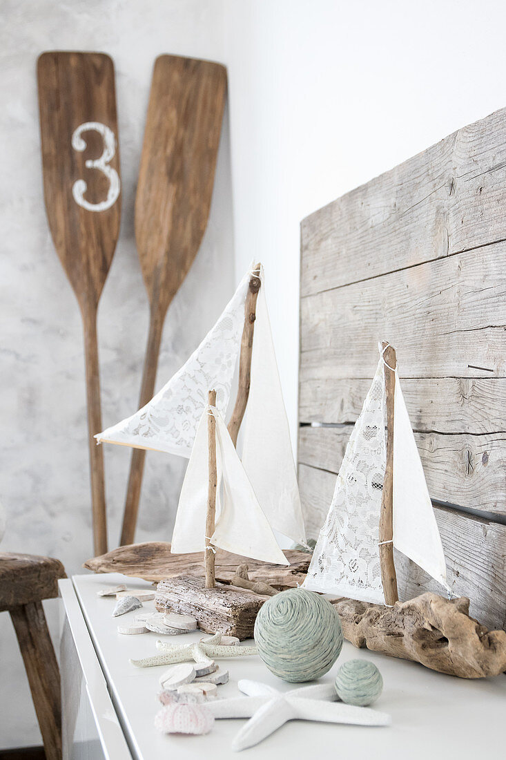 DIY-Segelboote aus Treibholz und Stoffresten und Paddel in Zimmerecke