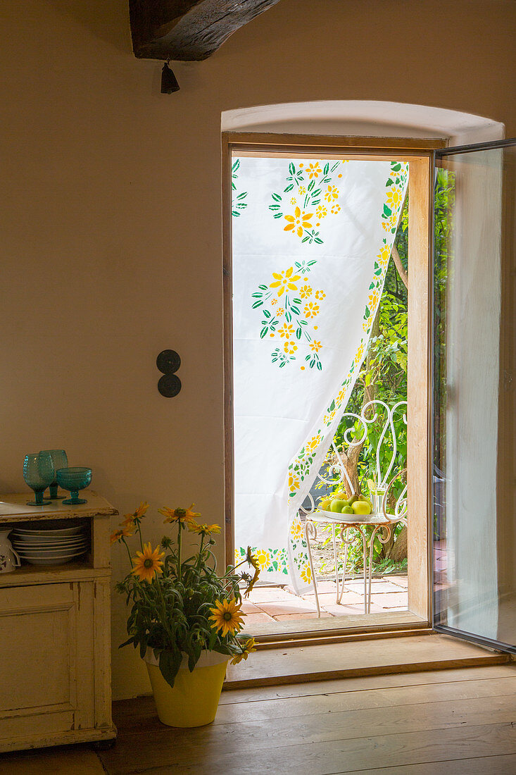 Mit Blumen bemalter Vorhang in der offenen Tür zum Landhaus