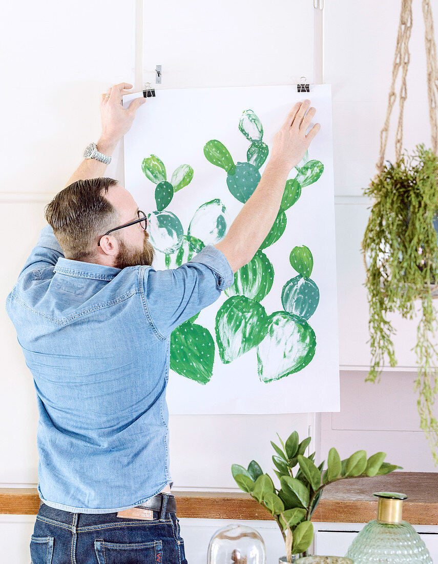 Mann hängt Poster mit aufgemaltem Kaktus auf