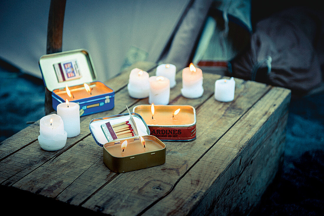 Kerzen in Blechdosen und Kerzenstumpen auf einer Holzkiste