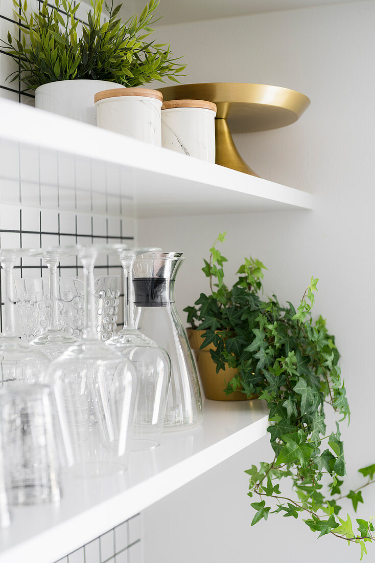 Houseplants and kitchen utensils on shelves against white-tiled kitchen wall
