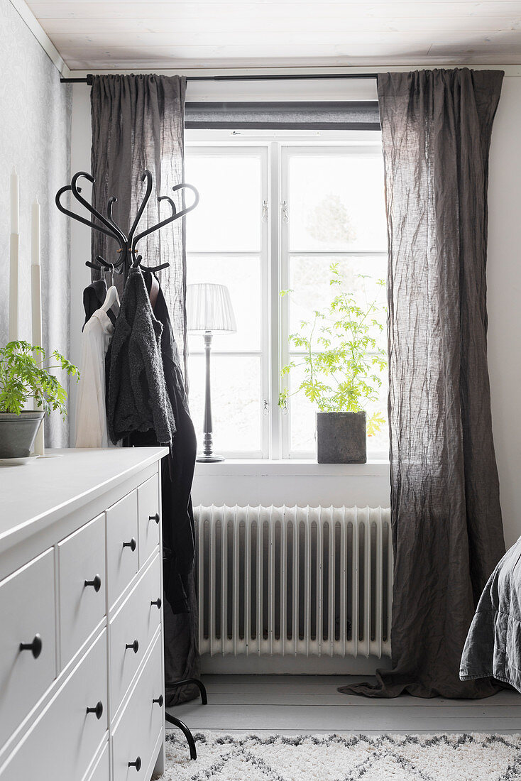 Weiße Schubladenkommode neben Kleiderständer am Fenster mit grauen Vorhängen