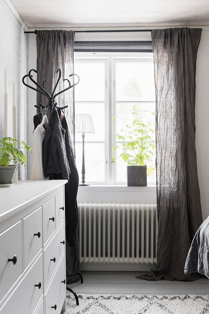 White chest of drawers next to coat stand and window with grey curtains