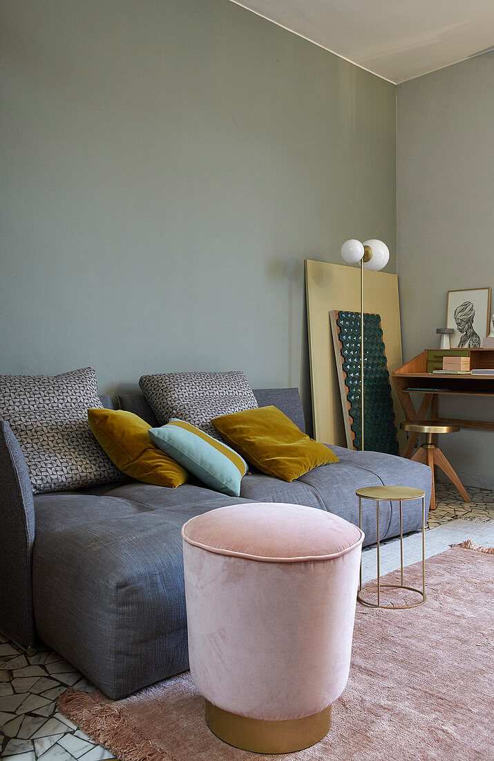 Pink velvet pouffe with brass base next to grey deep-seat sofa