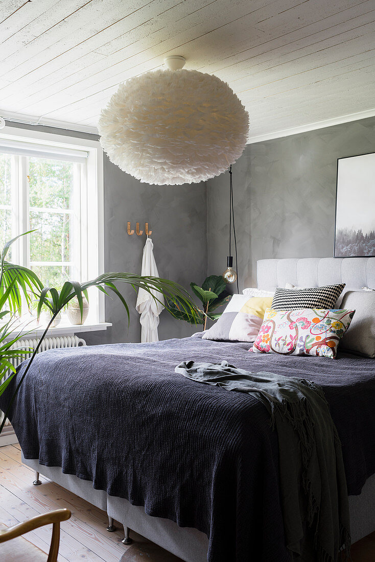 Dopllebett mit Kissensammlung und Lampe mit flauschigem Schirm im Schlafzimmer mit grauer Wand