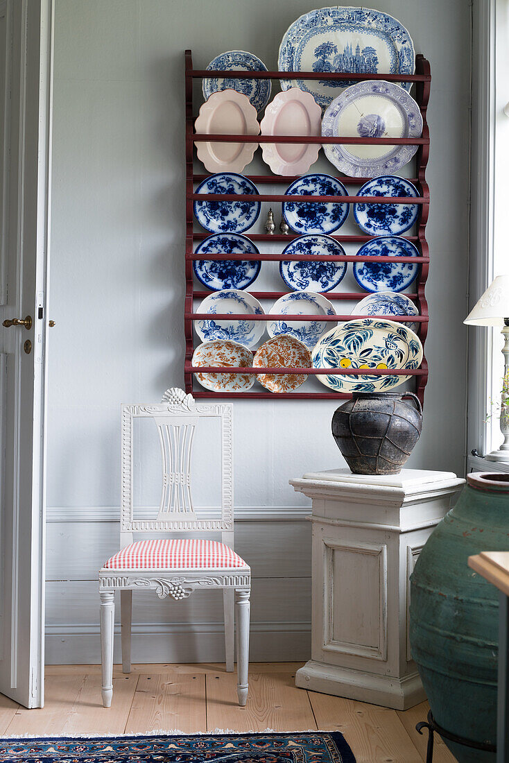 Plate rack, white chair and vase on wooden plinth in corner