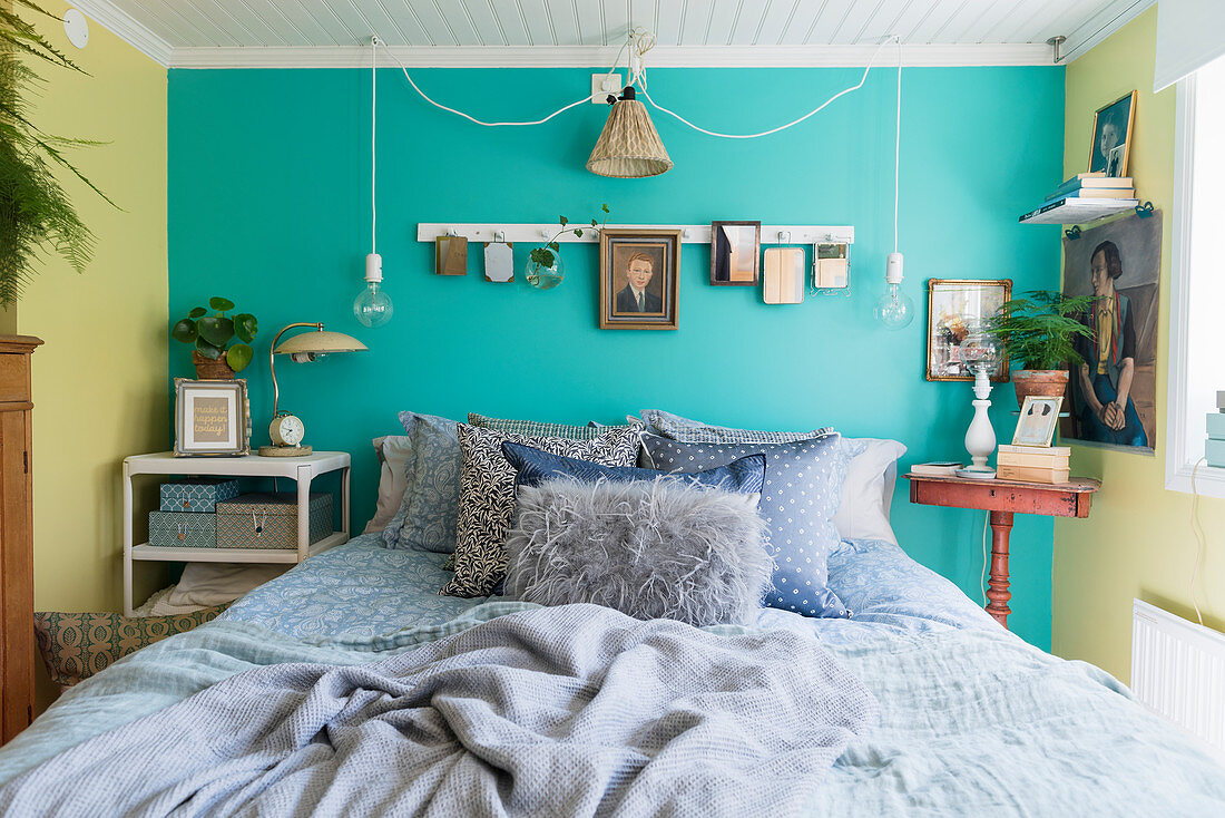 Schlafzimmer im nostalgischen Flair mit Bett vor türkisfarbener Wand