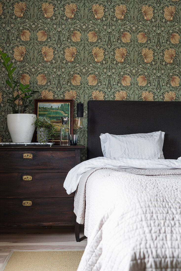 Double bed and bedside table against wall with William Morris wallpaper