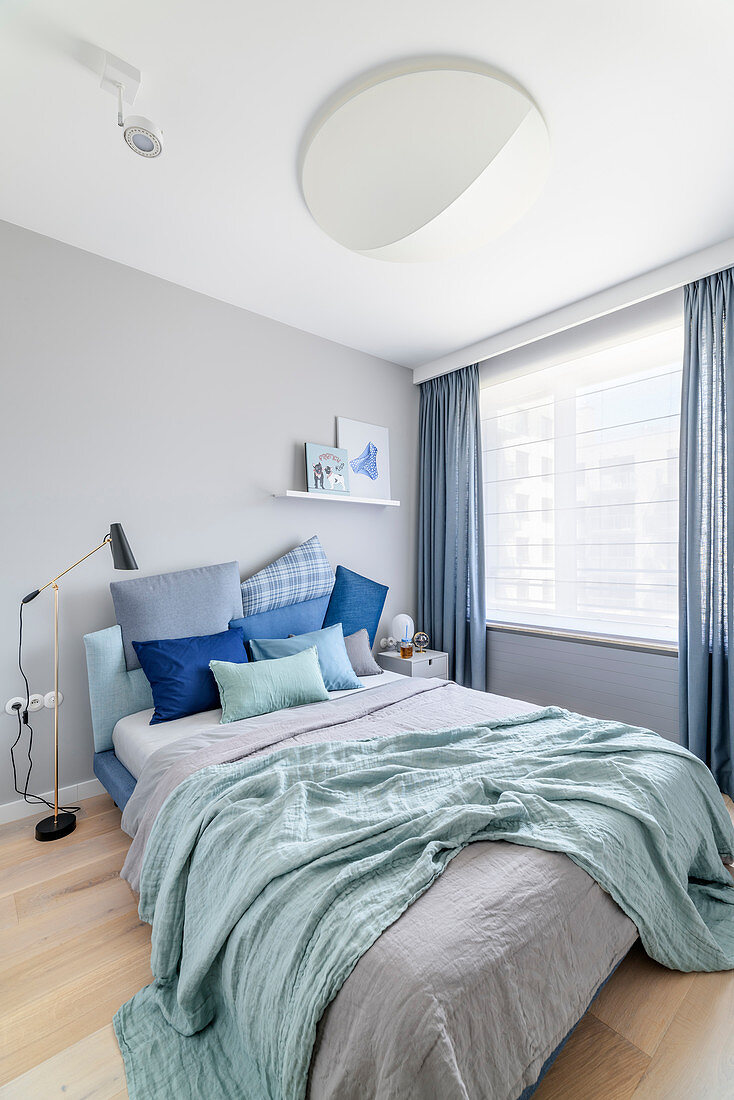 Kissen in Blautönen auf Doppelbett, im Schlafzimmer mit hellgrauen Wänden