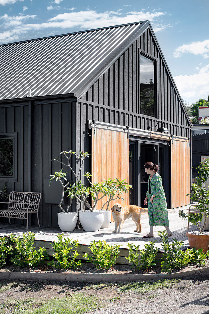 Frau und Hund auf der Terrasse vorm schwarzen Haus