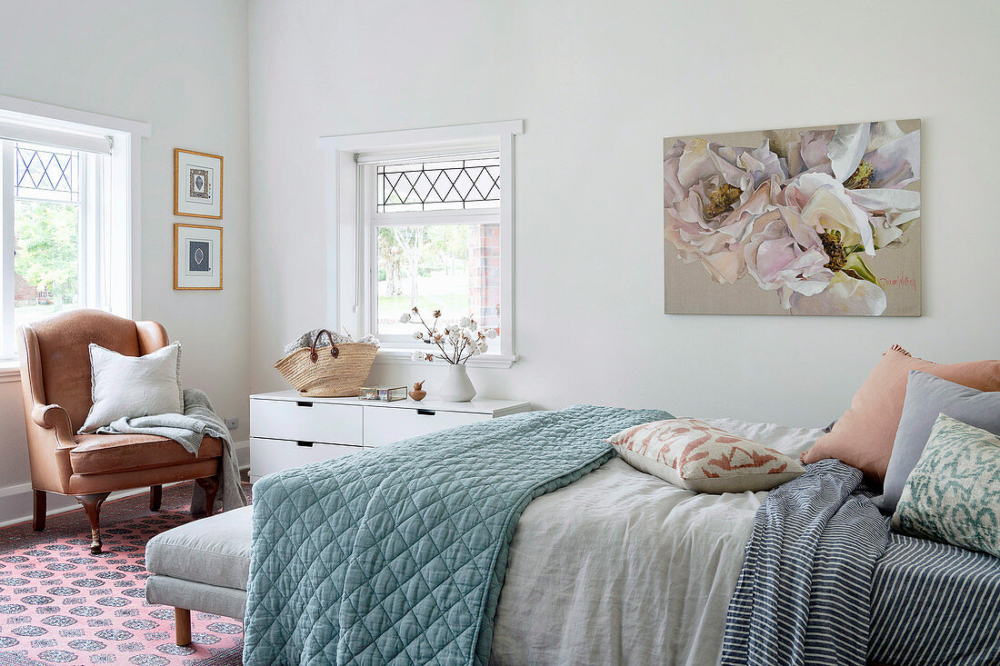 Doppelbett mit Kissen und Tagesdecke und antiker Ledersessel im Schlafzimmer