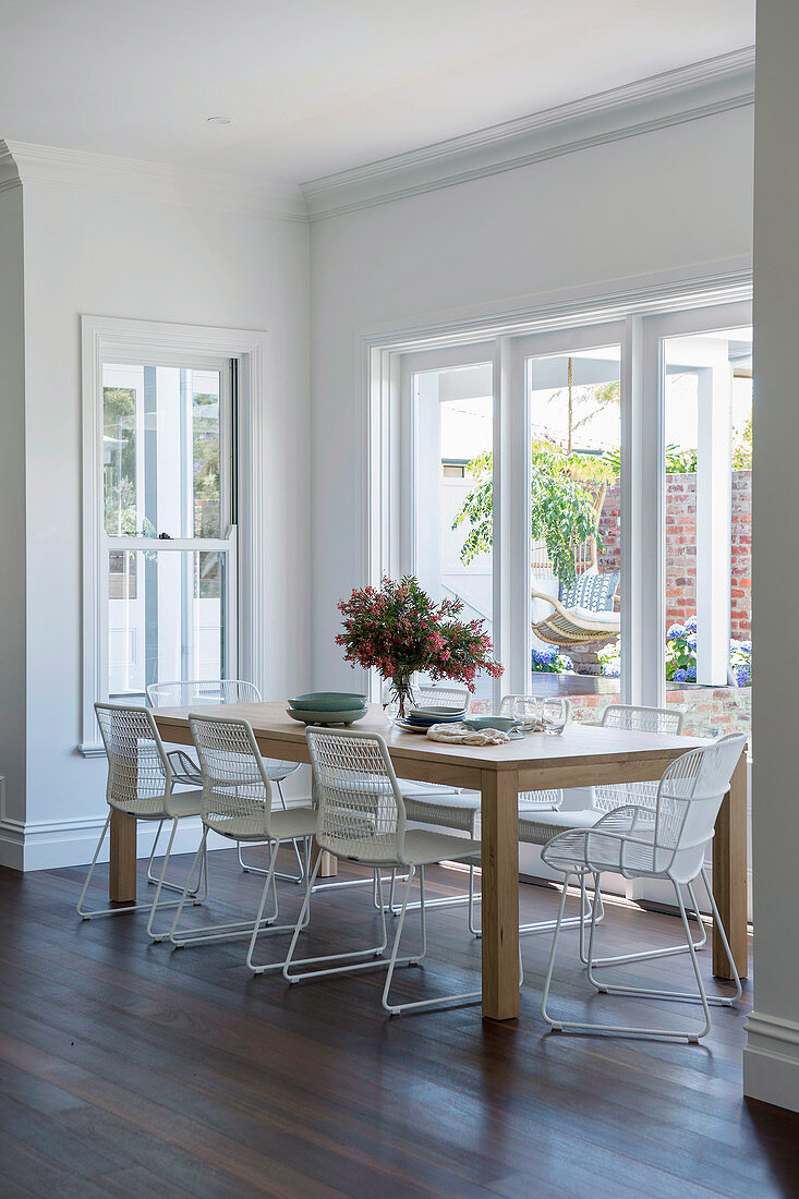 Filigrane weiße Stühle am Holztisch vorm Fenster zum Garten