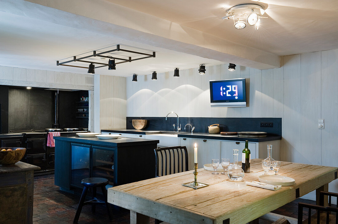 Schwarz-weiße Küche mit Kücheninsel, rustikalem Holztisch und verschiedenen Deckenstrahlern