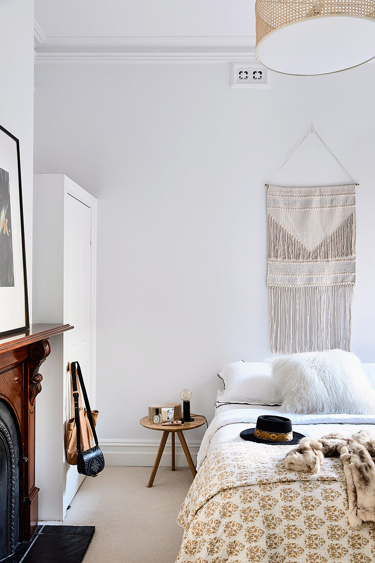 Bedroom in light beige tones with ethnic wall hangings over bed