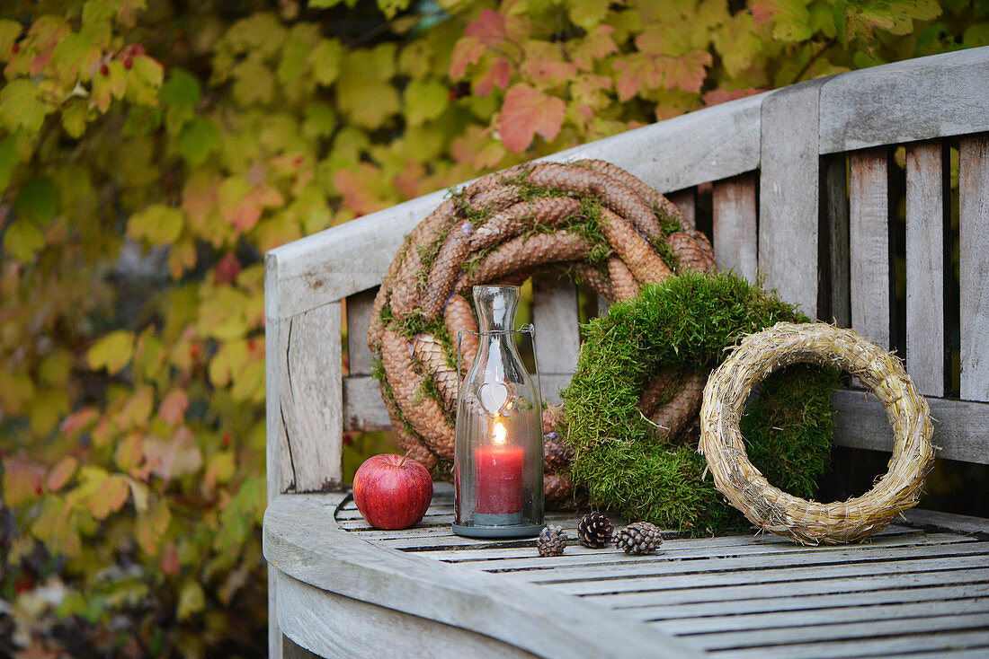 Garden bench decorated with wreaths (moss, fir cones and straw) and candle lantern
