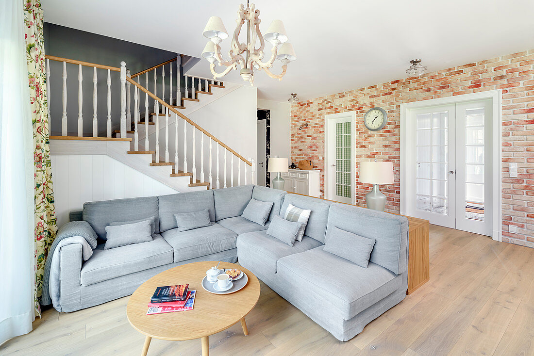 Grey sofa in open-plan interior with staircase and brick wall