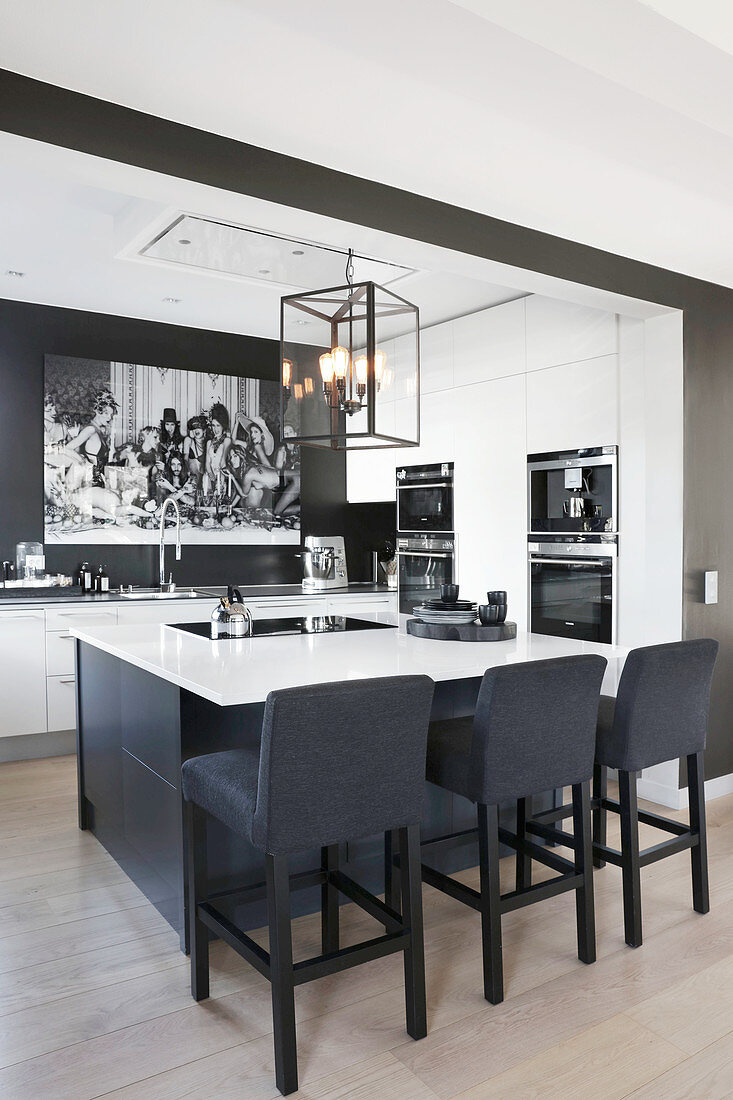 Island counter, fitted appliances and black wall in elegant, open-plan kitchen