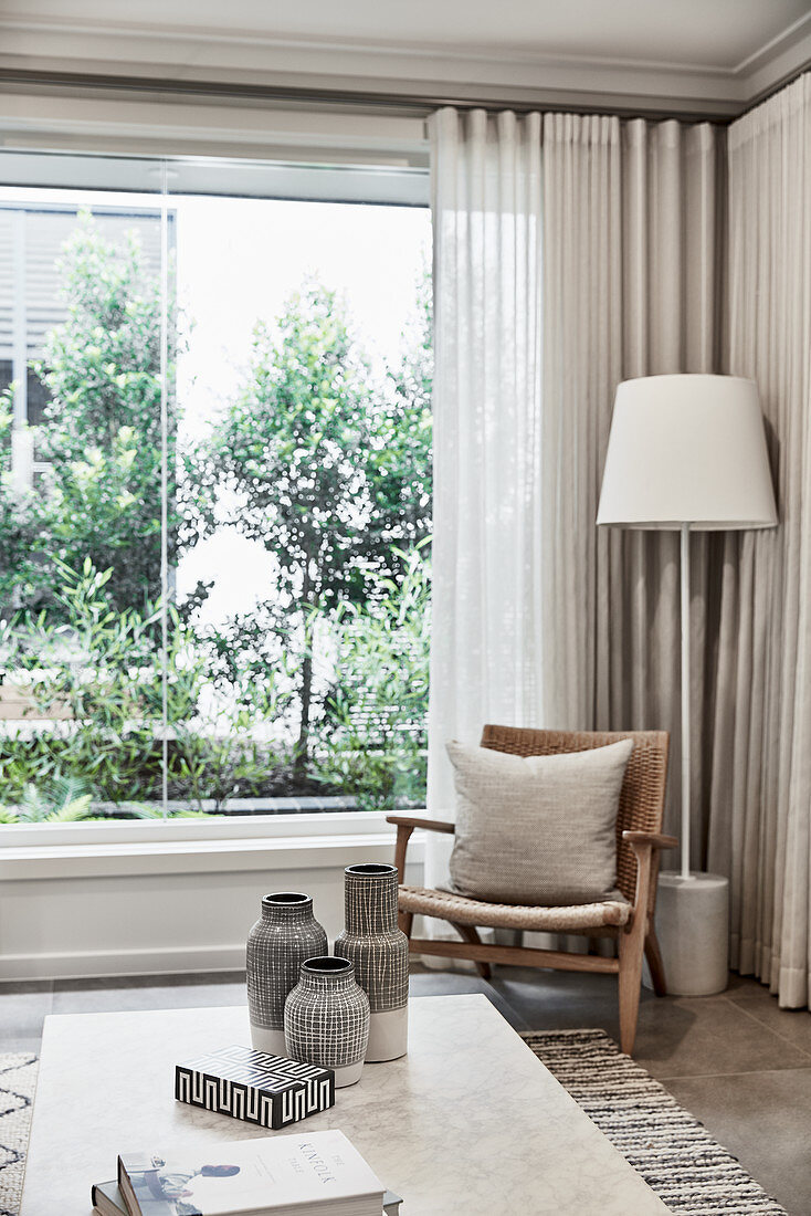 Rattanstuhl mit Kissen und Stehlampe vor Fenster mit bodenlangem Vorhang