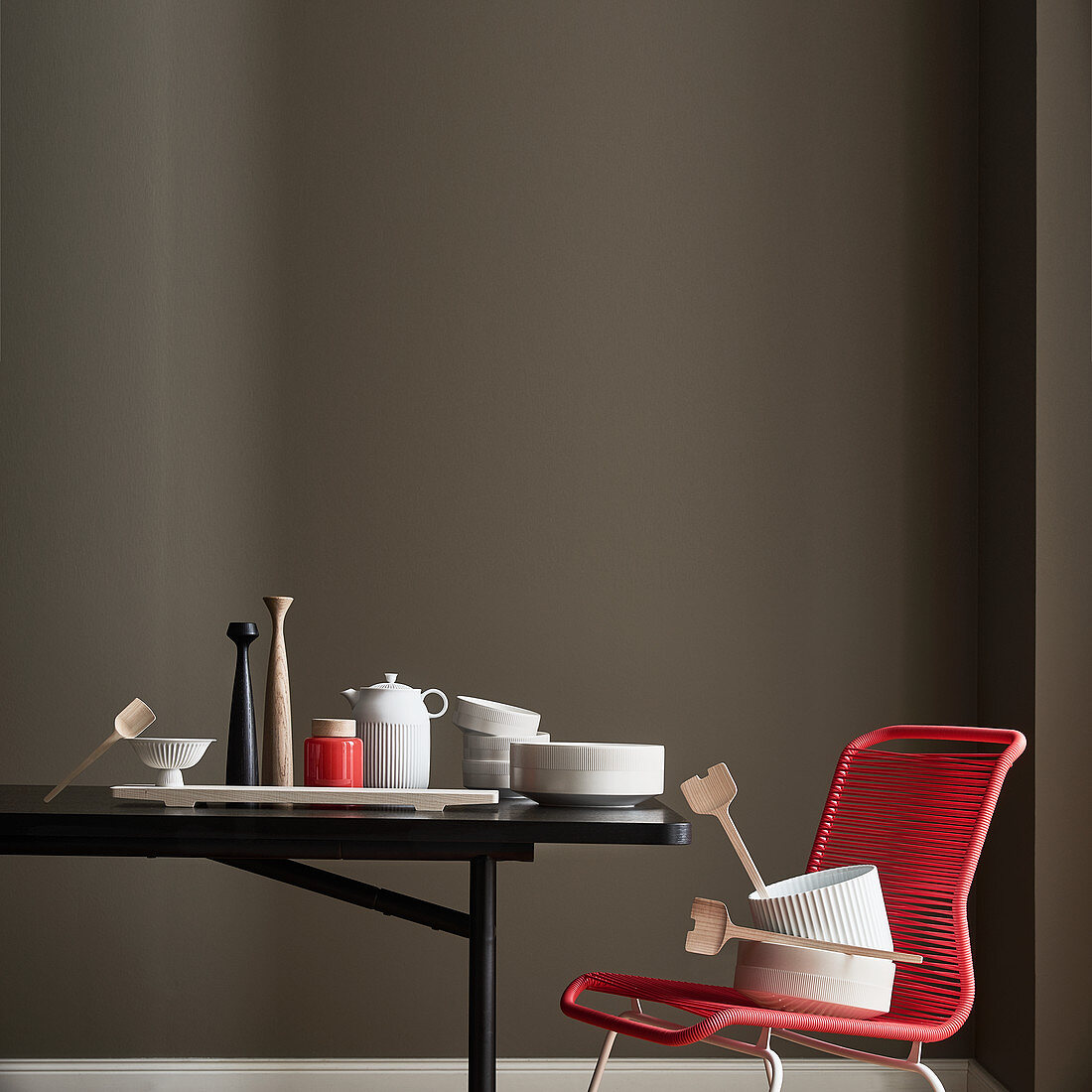 Schwarzer Tisch und roter Stuhl mit Geschirr vor dunkler Wand