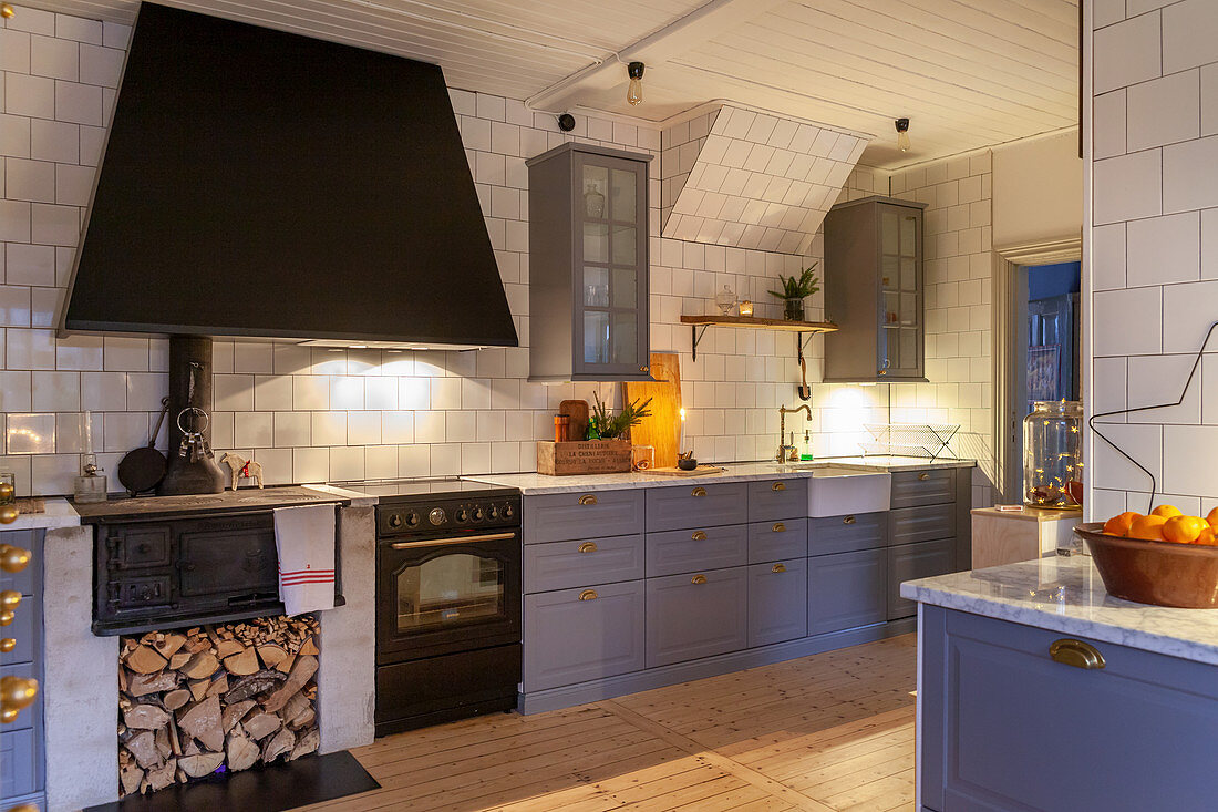 Moderne Landhausküche mit taubenblauen Schrankfronten, antikem Holzofenherd und weißen Fliesenwänden