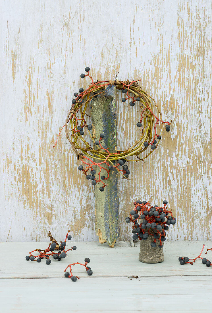 Gewundener Kranz aus Zweigen und Beeren des wilden Wein, darunter kleine Vase