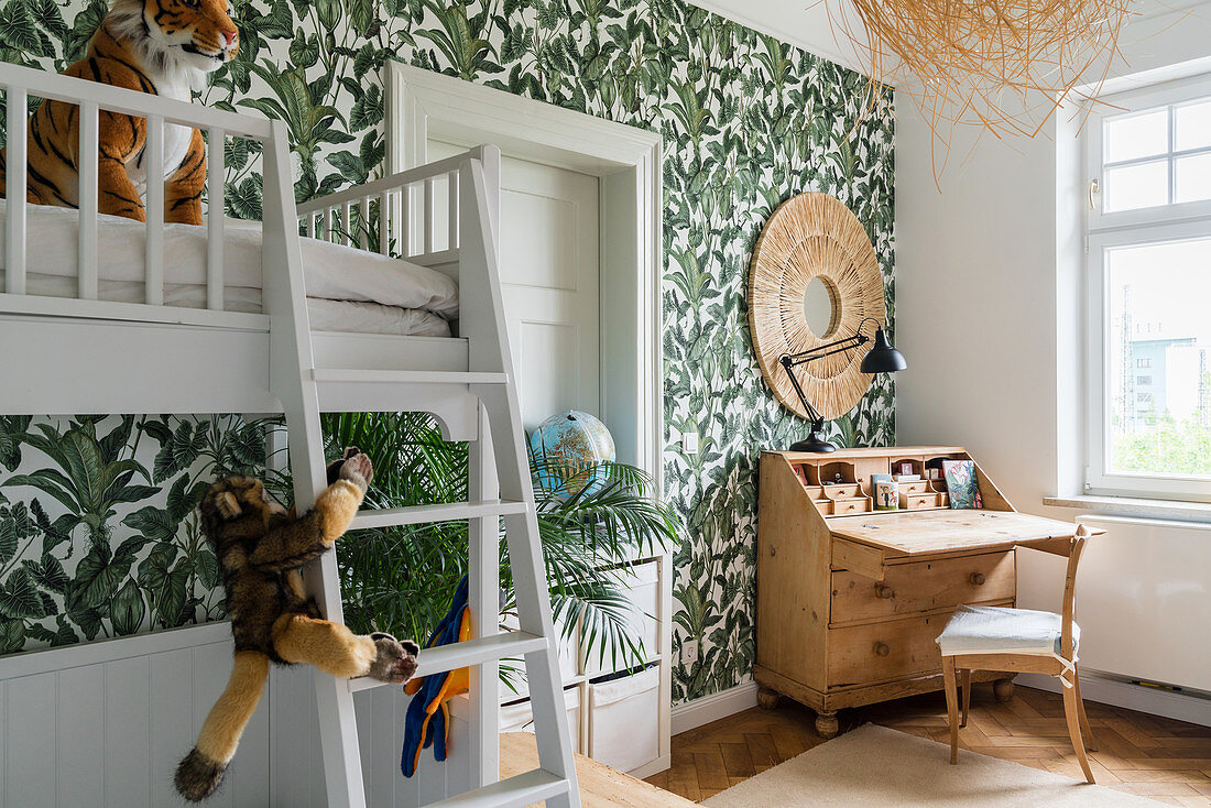 White bunk beds and wooden bureau in children's bedroom with jungle-patterned wallpaper