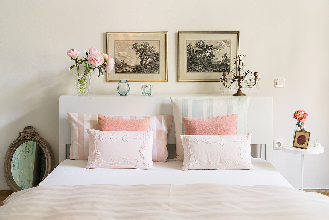 Double bed with white headboard used as shelf and pastel bed linen