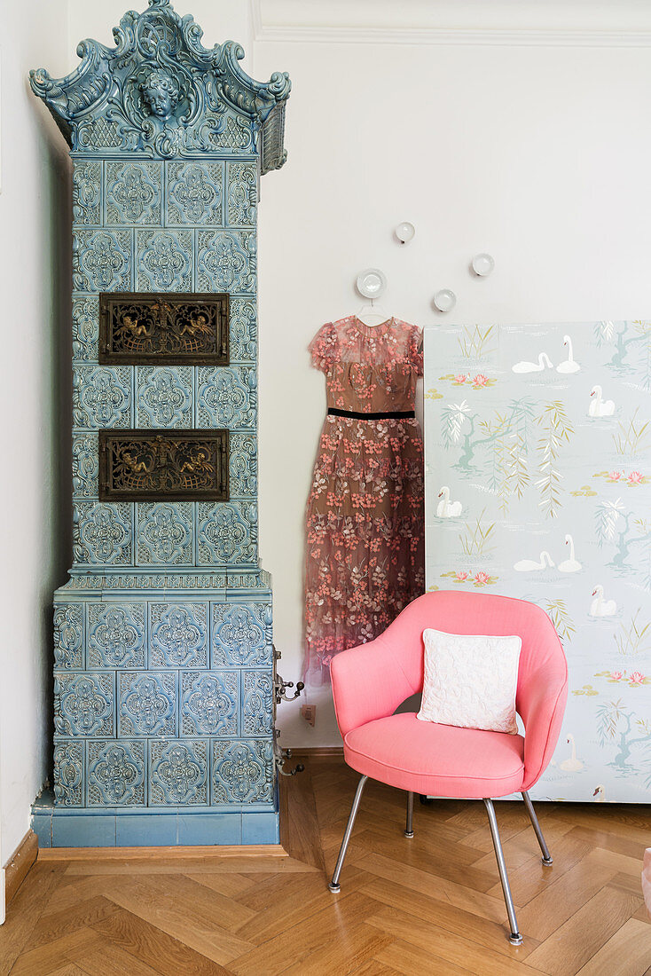 Kachelofen und rosa Stuhl vor Raumteiler mit Tapete im Schlafzimmer